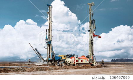 Drilling rig is actively working on a site to extract oil and gas resources. Workers are operating machinery under a bright sky with clouds in the background Drilling rig is actively working on a site to extract oil and gas resources. Workers are operating machinery under a bright sky with clouds in the background 136467099