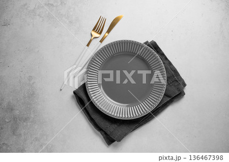 A ceramic dark gray plate with a cutlery and linen napkin on a concrete background. 136467398
