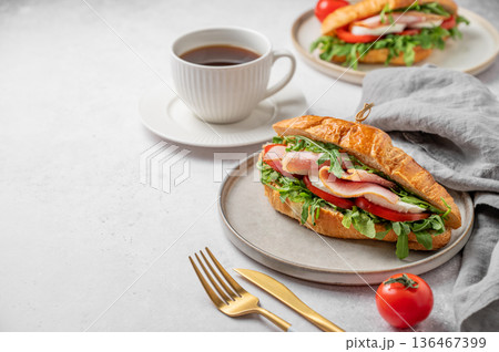 Croissant sandwich with ham, mozzarella cheese, tomato, arugula on a plate and cup of coffee Croissant sandwich with ham, mozzarella cheese, tomato, arugula on a plate and cup of coffee 136467399