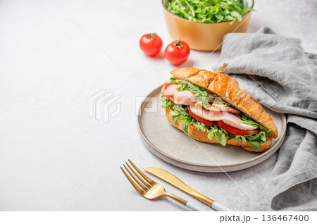 Croissant sandwich with ham, mozzarella cheese and arugula on a plate on a light background Croissant sandwich with ham, mozzarella cheese and arugula on a plate on a light background 136467400