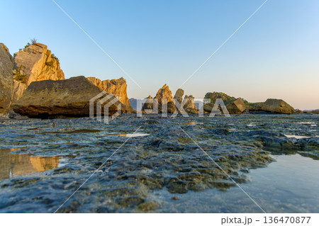 夕日に照らされる橋杭岩と干潮の岩場 136470877