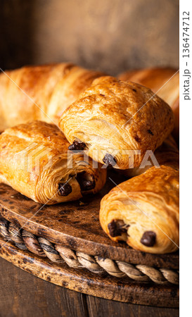 Freshly baked chocolate croissants arranged on a rustic wooden platter with warm tones 136474712