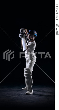 Junior cricket batsman holding bat in ready stance on black background. 136475114