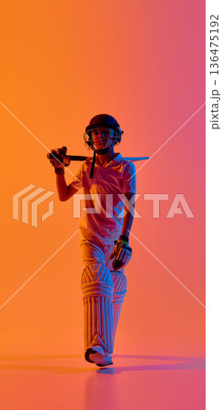 Young cricket player walking with bat on shoulder in neon gradient studio. Young cricket player walking with bat on shoulder in neon gradient studio. 136475192