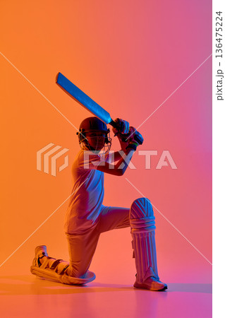 Cricket batsman kneeling with bat on vibrant orange purple background 136475224