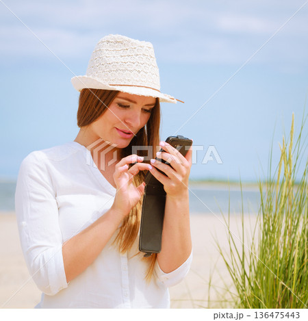 Woman on beach texting on smartphone. Woman on beach texting on smartphone. 136475443