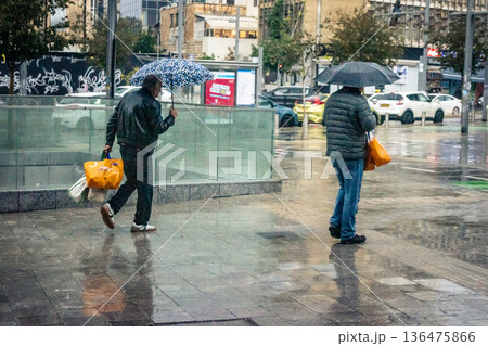 Pedestrians walk with umbrellas in the rain Pedestrians walk with umbrellas in the rain 136475866
