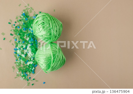 Green polyester yarn made from recycled plastic on a pile of microplastic flakes symbolizes sustainability, circular economy, and environmentally friendly production Green polyester yarn made from recycled plastic on a pile of microplastic flakes symbolizes sustainability, circular economy, and environmentally friendly production 136475904