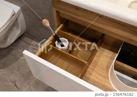 Wooden drawer reveals neatly arranged compartments, showcasing a makeup brush among other beauty essentials in a stylish bathroom Wooden drawer reveals neatly arranged compartments, showcasing a makeup brush among other beauty essentials in a stylish bathroom 136476182