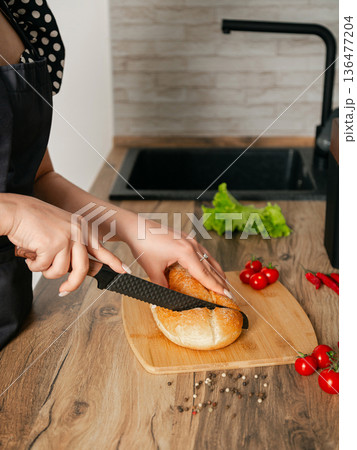 Girl cuts bread on a wooden board with a knife. Location of the kitchen. Girl cuts bread on a wooden board with a knife. Location of the kitchen. 136477204