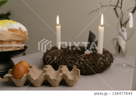 Festive Easter table with cake in white icing, painted eggs in tray, candles, and decorative twig nest centerpiece. Festive Easter table with cake in white icing, painted eggs in tray, candles, and decorative twig nest centerpiece. 136477645