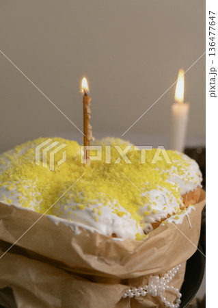 Easter cake on table with white icing and yellow coconut sprinkles, lit candle nearby, creating festive Easter atmosphere. Easter cake on table with white icing and yellow coconut sprinkles, lit candle nearby, creating festive Easter atmosphere. 136477647