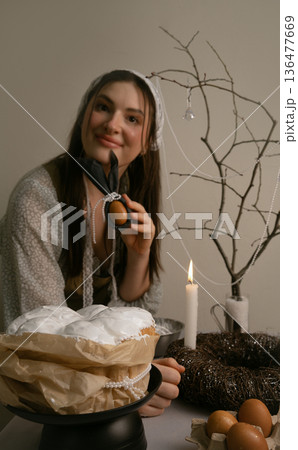 Preparing for Easter evening, she decorates the table with colorful eggs and candles, creating cozy festive atmosphere. Preparing for Easter evening, she decorates the table with colorful eggs and candles, creating cozy festive atmosphere. 136477669