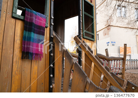 Wool plaid scarf hanging on a small playground house outdoors. Everyday scene showing a personal clothing item left in a public play area, with a casual, real-life feel. Wool plaid scarf hanging on a small playground house outdoors. Everyday scene showing a personal clothing item left in a public play area, with a casual, real-life feel. 136477670