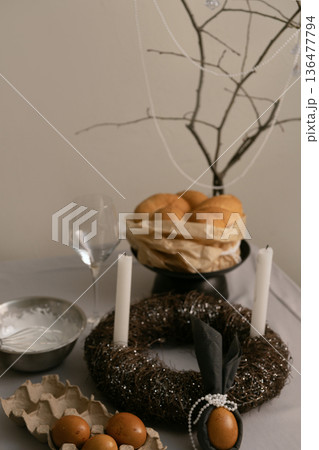 On festive Easter table, cake decorated with white icing, with eggs in tray, candles, and twig wreath nearby. 136477794