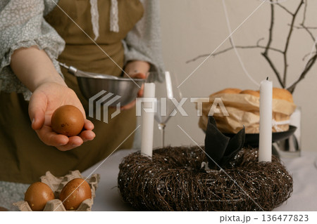 In home clothes, she lovingly prepares the Easter table, creating coziness and a warm family celebration atmosphere. In home clothes, she lovingly prepares the Easter table, creating coziness and a warm family celebration atmosphere. 136477823