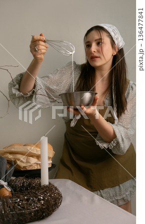 Easter holiday feeling woman in apron making glaze for cake at beautifully set festive table 136477841