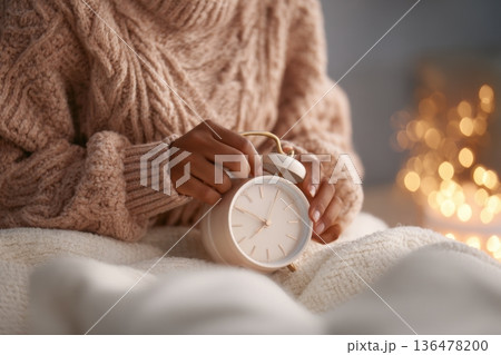 Hands gently adjust the dial of a classic alarm clock, creating a peaceful bedtime ritual in a cozy and inviting room 136478200