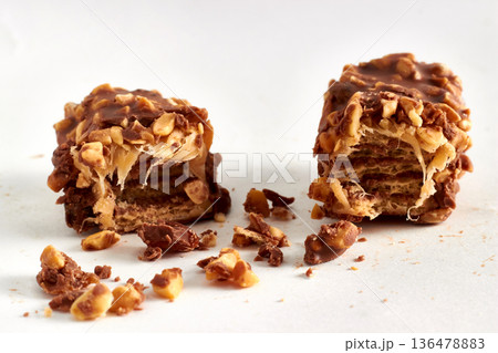 Close-up of a broken chocolate caramel bar with nuts on a white background. 136478883