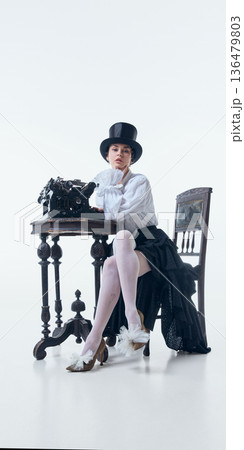 Woman in top hat sitting at antique desk with typewriter in poetcore style. Woman in top hat sitting at antique desk with typewriter in poetcore style. 136479803