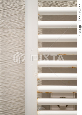 White bathroom towel rail radiator showing signs of rust and corrosion, indicating metal degradation and the need for home maintenance or a plumbing repair White bathroom towel rail radiator showing signs of rust and corrosion, indicating metal degradation and the need for home maintenance or a plumbing repair 136479877
