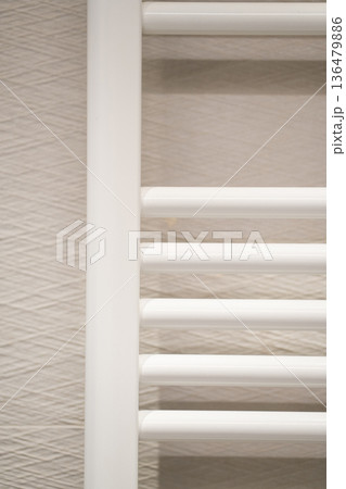 White towel radiator installed on a textured light beige wall in a modern bathroom, providing warmth and a practical drying solution 136479886