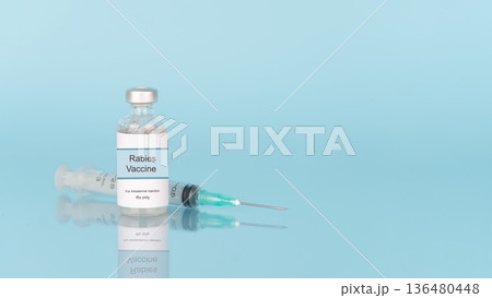 Rabies vaccine bottle and syringe on blue background with reflection. Vaccine used to prevent rabies virus infection. Rabies vaccine bottle and syringe on blue background with reflection. Vaccine used to prevent rabies virus infection. 136480448
