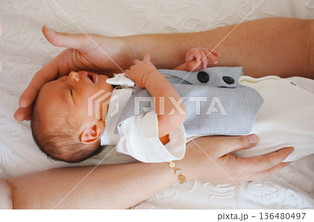 Baby dressed in suit lies on adult's lap in soft light Baby dressed in suit lies on adult's lap in soft light 136480497
