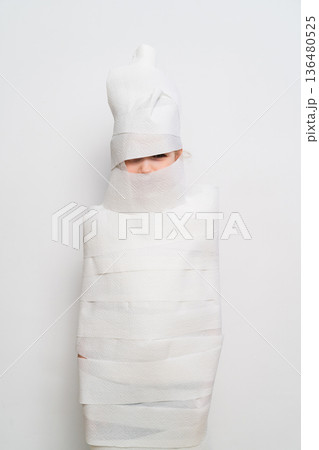 Person wrapped in strips of white material in a plain space Person wrapped in strips of white material in a plain space 136480525