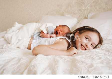 Sister smiles while lying with newborn baby on bed 136480691