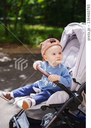 Child enjoys sunny day in stroller at local park 136480793