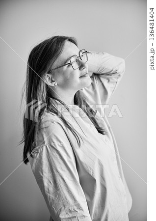 Side view of young female happily smiling and looking away. Portrait of lovely girl in cream shirt standing in natural light. Black and white image. Side view of young female happily smiling and looking away. Portrait of lovely girl in cream shirt standing in natural light. Black and white image. 136481404