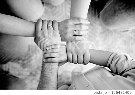 Top view of family hands holding each others wrists in circle, creating chain of support or unity. Concept of connection, teamwork, family, strength, trust. Black and white image 136481409