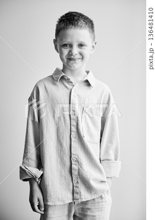 Portrait of happy boy in casual clothes keeping hand in pocket. Adorable boy smiling to camera. Stylish kid posing on white background. Black and white image. 136481410