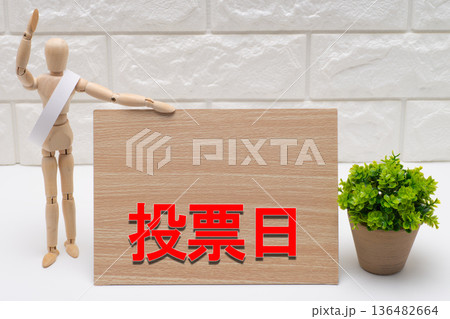 タスキを掛けた選挙の候補者と投票日を示す看板 136482664
