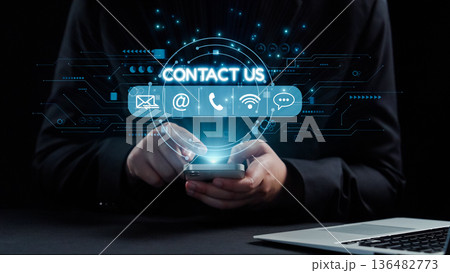 Hands holding smartphone with glowing digital contact icons and futuristic interface elements against dark background for communication and connection solutions. Qubit 136482773