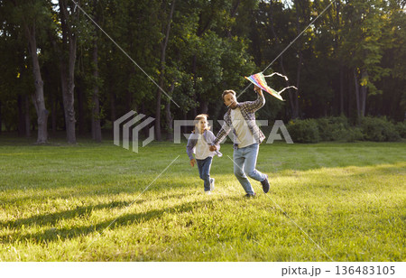 Happy father and child running in park, flying colorful kite and enjoying fun outdoor time together. 136483105