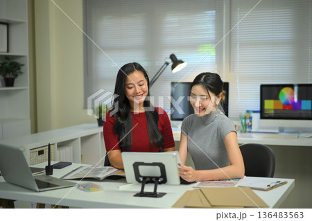 Young women discussing graphic design work at office desk, creative teamwork, planning ideas and modern workplace collaboration. Young women discussing graphic design work at office desk, creative teamwork, planning ideas and modern workplace collaboration. 136483563