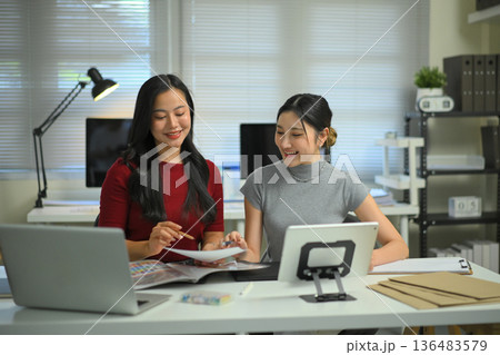 Young women discussing graphic design work at office desk, creative teamwork, planning ideas and modern workplace collaboration. Young women discussing graphic design work at office desk, creative teamwork, planning ideas and modern workplace collaboration. 136483579