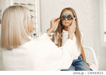 Child eye test and eye exam. Little girl having eye check-up, with phoropter. Doctor performs eye test for child. 136483615