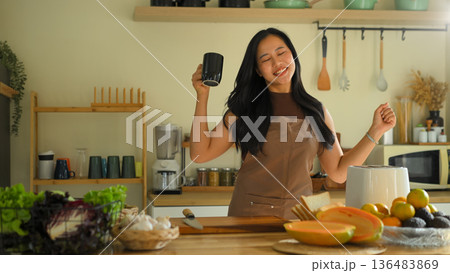 Happy woman dancing while preparing healthy breakfast in a cozy kitchen, enjoying morning routine Happy woman dancing while preparing healthy breakfast in a cozy kitchen, enjoying morning routine 136483869