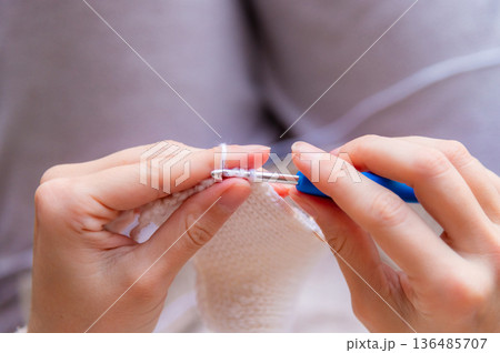 A close-up of a young Caucasian woman's hands crocheting a woolen item at home. A pleasant, meditative hobby. 136485707