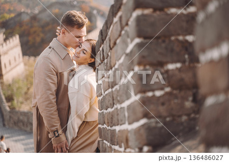 beautiful young couple hugging at the Great Wall of China. Newly married couple on their honemoon to Great Wall near Beijing China. Stylish couple exploring one of the wonders of the world. beautiful young couple hugging at the Great Wall of China. Newly married couple on their honemoon to Great Wall near Beijing China. Stylish couple exploring one of the wonders of the world. 136486027