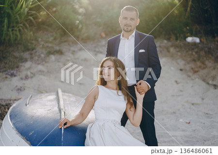beautiful young long-haired bride in white dress with her young husband on the beach beautiful young long-haired bride in white dress with her young husband on the beach 136486061