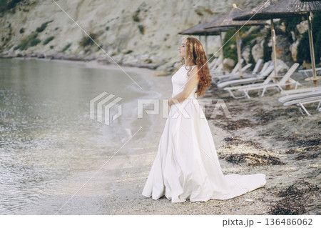 Beautiful long-haired bride in a magnificent white dress walking on a beach Beautiful long-haired bride in a magnificent white dress walking on a beach 136486062
