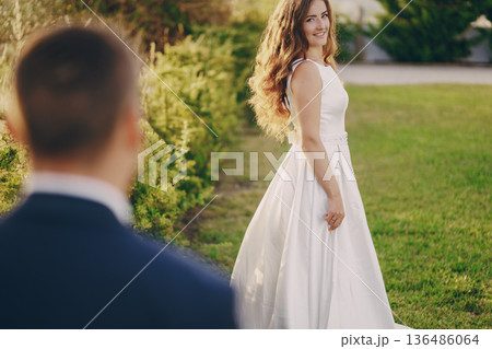 beautiful long-haired bride in white dress with her young man walking in the nature beautiful long-haired bride in white dress with her young man walking in the nature 136486064