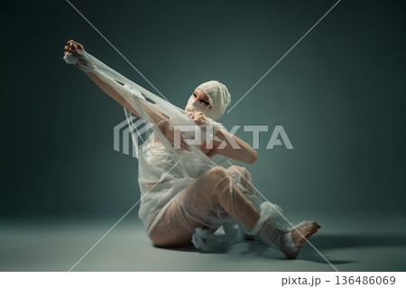 Conceptual art of a person wrapped in bandages struggling to break free from confinement. 136486069