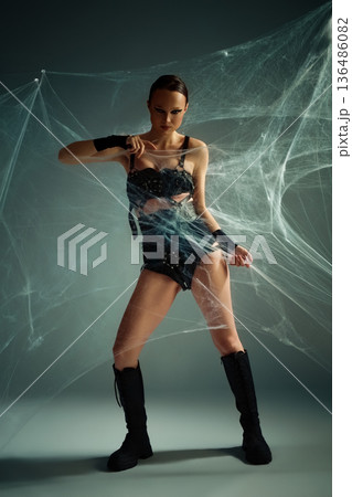 Powerful woman in black gothic costume tangled in a studio spiderweb 136486082