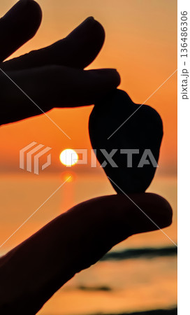 Holding a heart-shaped stone against the backdrop of a sunset over the water creating a moment of connection and reflection Holding a heart-shaped stone against the backdrop of a sunset over the water creating a moment of connection and reflection 136486306