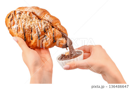 Croissant dipped in chocolate spread in female hands isolated on white Croissant dipped in chocolate spread in female hands isolated on white 136486647